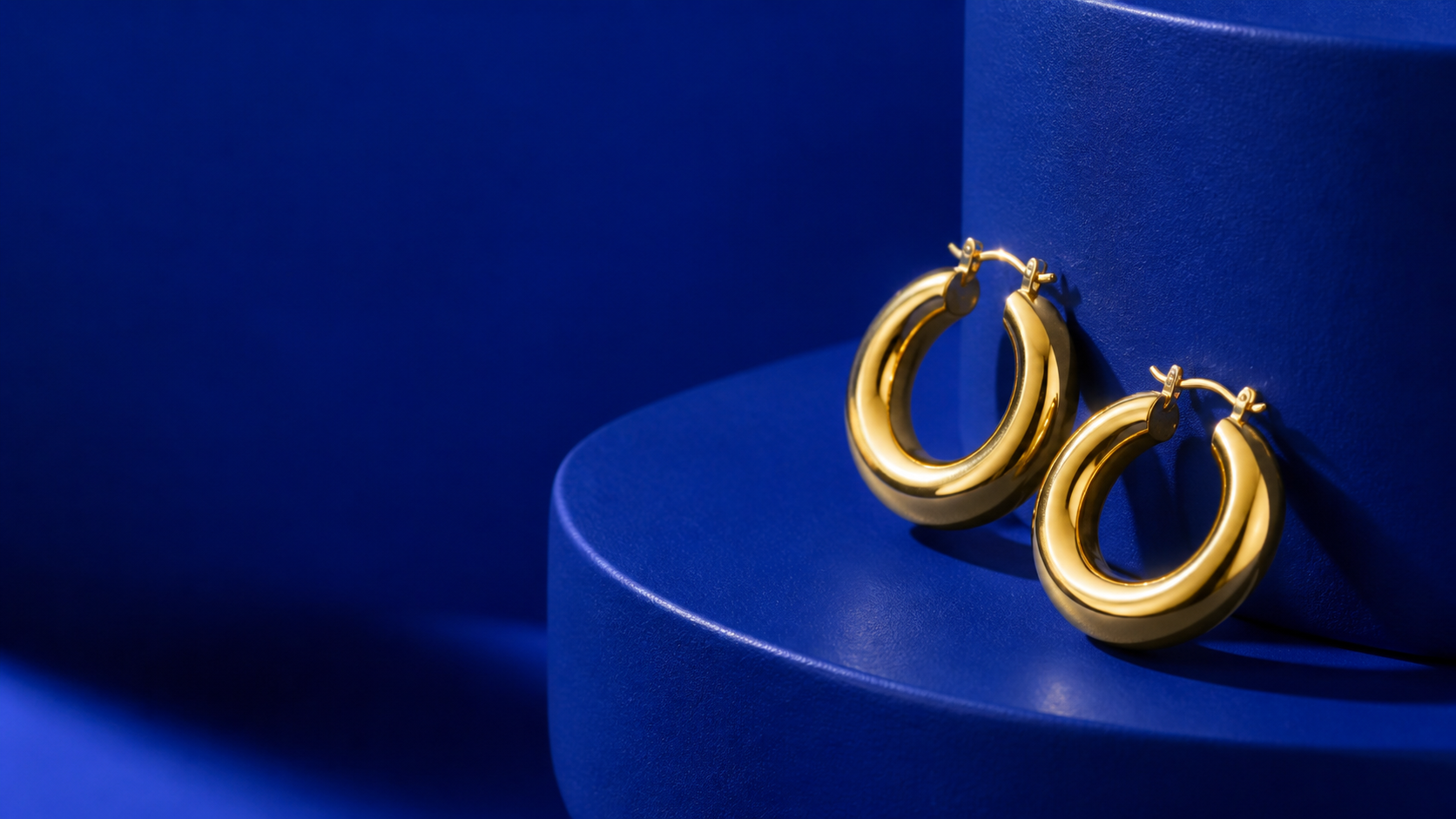 AUWE gold hoop earrings on cobalt blue